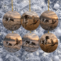 Six round ceramic Christmas ornaments hanging on a frosted Christmas tree. Each ornament features a print of a German Shorthair Pointer flushing  in a frosty field at sunset.