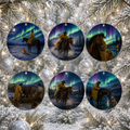 Six round ceramic Christmas ornaments hanging on a snowy pine tree, each featuring a western-style scene with cowboys on horseback under the aurora borealis.